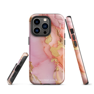 The Gold Blush Marble for iPhone showcases a glossy, marble-patterned case in shades of pink and gold. The decorative design features swirling patterns, seamlessly blending the colors. Crafted with impact-resistant polycarbonate for superior phone protection, "Statement Cases" is written in white at the bottom.