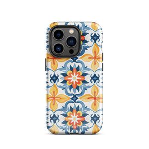 Statement Cases' Mediterranean Bloom for iPhone is showcased, featuring an intricate, colorful pattern. The design includes blue, yellow, and orange floral shapes in a symmetrical arrangement on a light blue background. This durable phone case provides dual-layer protection and is constructed from impact-resistant polycarbonate to safeguard your device.