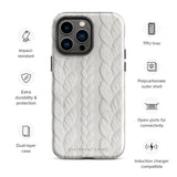 The Cozy Knit Bliss for iPhone by Statement Cases is designed for a smartphone with three rear cameras. It offers dual-layer protection and features a textured white pattern that looks like knitted fabric. The bottom of the case has the text "STATEMENT CASES" engraved, ensuring both style and impact-resistant durability.