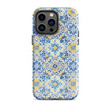 The Blue Mirage for iPhone by Statement Cases features a dual-layered, impact-resistant polycarbonate exterior with a TPU inner liner. Inspired by traditional Portuguese tiles, the blue and yellow patterned case boasts an intricate design of floral and geometric motifs. With its elegant and colorful appearance, the phone's camera is visible at the top left of the case.