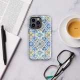 The Blue Mirage for iPhone by Statement Cases features a dual-layered, impact-resistant polycarbonate exterior with a TPU inner liner. Inspired by traditional Portuguese tiles, the blue and yellow patterned case boasts an intricate design of floral and geometric motifs. With its elegant and colorful appearance, the phone's camera is visible at the top left of the case.