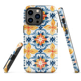 Statement Cases' Mediterranean Bloom for iPhone is showcased, featuring an intricate, colorful pattern. The design includes blue, yellow, and orange floral shapes in a symmetrical arrangement on a light blue background. This durable phone case provides dual-layer protection and is constructed from impact-resistant polycarbonate to safeguard your device.