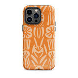 A Savannah Ardiente for iPhone from Statement Cases, featuring a dual-layered phone case in orange with a floral pattern showcasing cream-colored flowers, leaves, and geometric shapes. This impact-resistant polycarbonate case displays "STATEMENT CASES" at the bottom and reveals the camera lenses at the top left corner.