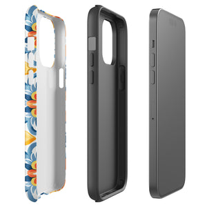 Statement Cases' Mediterranean Bloom for iPhone is showcased, featuring an intricate, colorful pattern. The design includes blue, yellow, and orange floral shapes in a symmetrical arrangement on a light blue background. This durable phone case provides dual-layer protection and is constructed from impact-resistant polycarbonate to safeguard your device.