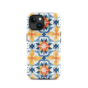 Statement Cases' Mediterranean Bloom for iPhone is showcased, featuring an intricate, colorful pattern. The design includes blue, yellow, and orange floral shapes in a symmetrical arrangement on a light blue background. This durable phone case provides dual-layer protection and is constructed from impact-resistant polycarbonate to safeguard your device.