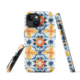 Statement Cases' Mediterranean Bloom for iPhone is showcased, featuring an intricate, colorful pattern. The design includes blue, yellow, and orange floral shapes in a symmetrical arrangement on a light blue background. This durable phone case provides dual-layer protection and is constructed from impact-resistant polycarbonate to safeguard your device.