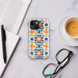 Statement Cases' Mediterranean Bloom for iPhone is showcased, featuring an intricate, colorful pattern. The design includes blue, yellow, and orange floral shapes in a symmetrical arrangement on a light blue background. This durable phone case provides dual-layer protection and is constructed from impact-resistant polycarbonate to safeguard your device.