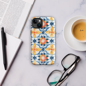 Statement Cases' Mediterranean Bloom for iPhone is showcased, featuring an intricate, colorful pattern. The design includes blue, yellow, and orange floral shapes in a symmetrical arrangement on a light blue background. This durable phone case provides dual-layer protection and is constructed from impact-resistant polycarbonate to safeguard your device.