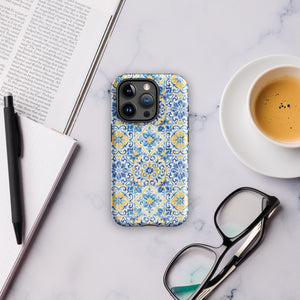 The Blue Mirage for iPhone by Statement Cases features a dual-layered, impact-resistant polycarbonate exterior with a TPU inner liner. Inspired by traditional Portuguese tiles, the blue and yellow patterned case boasts an intricate design of floral and geometric motifs. With its elegant and colorful appearance, the phone's camera is visible at the top left of the case.