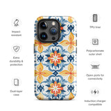 Statement Cases' Mediterranean Bloom for iPhone is showcased, featuring an intricate, colorful pattern. The design includes blue, yellow, and orange floral shapes in a symmetrical arrangement on a light blue background. This durable phone case provides dual-layer protection and is constructed from impact-resistant polycarbonate to safeguard your device.