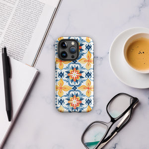 Statement Cases' Mediterranean Bloom for iPhone is showcased, featuring an intricate, colorful pattern. The design includes blue, yellow, and orange floral shapes in a symmetrical arrangement on a light blue background. This durable phone case provides dual-layer protection and is constructed from impact-resistant polycarbonate to safeguard your device.