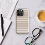 A stylish smartphone with an Au Naturale for iPhone, beige and white striped, durable dual-layered case rests on a marble surface. Nearby are a pen, an open notebook, a pair of glasses, a partially visible magazine, and a cup of espresso on a white saucer. The case is branded "Statement Cases.
