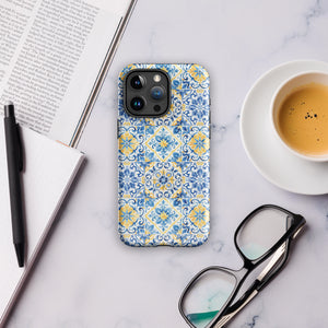 The Blue Mirage for iPhone by Statement Cases features a dual-layered, impact-resistant polycarbonate exterior with a TPU inner liner. Inspired by traditional Portuguese tiles, the blue and yellow patterned case boasts an intricate design of floral and geometric motifs. With its elegant and colorful appearance, the phone's camera is visible at the top left of the case.