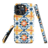 Statement Cases' Mediterranean Bloom for iPhone is showcased, featuring an intricate, colorful pattern. The design includes blue, yellow, and orange floral shapes in a symmetrical arrangement on a light blue background. This durable phone case provides dual-layer protection and is constructed from impact-resistant polycarbonate to safeguard your device.