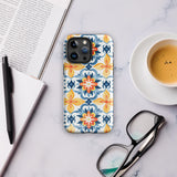 Statement Cases' Mediterranean Bloom for iPhone is showcased, featuring an intricate, colorful pattern. The design includes blue, yellow, and orange floral shapes in a symmetrical arrangement on a light blue background. This durable phone case provides dual-layer protection and is constructed from impact-resistant polycarbonate to safeguard your device.