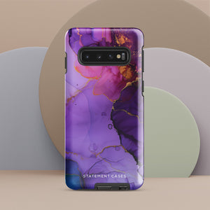 The Golden Orchid Marble for Samsung by Statement Cases is a smartphone adorned with a vibrant, abstract phone case showcasing a mix of purple, pink, and gold colors. Crafted from impact-resistant materials, it features a camera module with four lenses and a flash. At the bottom of the shock-absorbing phone case, you’ll find the text "STATEMENT CASES" in white.