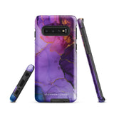 The Golden Orchid Marble for Samsung by Statement Cases is a smartphone adorned with a vibrant, abstract phone case showcasing a mix of purple, pink, and gold colors. Crafted from impact-resistant materials, it features a camera module with four lenses and a flash. At the bottom of the shock-absorbing phone case, you’ll find the text "STATEMENT CASES" in white.