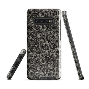 A phone case with a protective dual-layer design featuring an intricate black floral lace pattern. The Omerta Floral for Samsung has four camera cutouts and the brand name "Statement Cases" appears at the bottom center. Impact-resistant and chic, it stands against a plain white background.