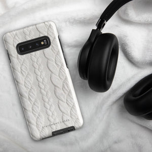 A stylish, impact-resistant phone case with a textured white braided design, covering the back of a smartphone. The dual-layer design features cutouts for the camera and buttons, and "Cozy Knit Bliss for Samsung" by Statement Cases is embossed at the bottom.