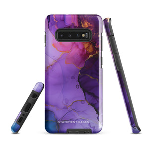 The Golden Orchid Marble for Samsung by Statement Cases is a smartphone adorned with a vibrant, abstract phone case showcasing a mix of purple, pink, and gold colors. Crafted from impact-resistant materials, it features a camera module with four lenses and a flash. At the bottom of the shock-absorbing phone case, you’ll find the text "STATEMENT CASES" in white.