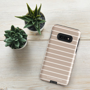 A Au Naturale for Samsung with a beige and white striped, dual-layer design case lies on a light wooden surface. Beside the phone are three small potted succulent plants, adding a touch of greenery to the minimalistic scene. The bottom of the impact-resistant phone case features the brand name "Statement Cases.