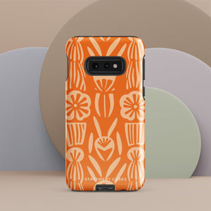 This stylish smartphone accessory, the Savannah Ardiente for Samsung by Statement Cases, features a shock-absorbing, colorful patterned case adorned with abstract flower designs in beige on an orange background. This impact-resistant phone case wraps around the back of your device, providing robust protection for its multiple camera lenses in the corner.