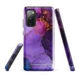 The Golden Orchid Marble for Samsung by Statement Cases is a smartphone adorned with a vibrant, abstract phone case showcasing a mix of purple, pink, and gold colors. Crafted from impact-resistant materials, it features a camera module with four lenses and a flash. At the bottom of the shock-absorbing phone case, you’ll find the text "STATEMENT CASES" in white.