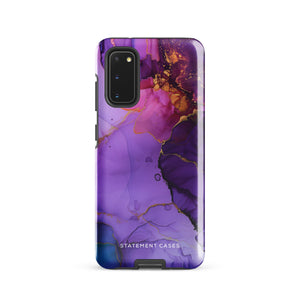 The Golden Orchid Marble for Samsung by Statement Cases is a smartphone adorned with a vibrant, abstract phone case showcasing a mix of purple, pink, and gold colors. Crafted from impact-resistant materials, it features a camera module with four lenses and a flash. At the bottom of the shock-absorbing phone case, you’ll find the text "STATEMENT CASES" in white.