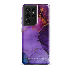 The Golden Orchid Marble for Samsung by Statement Cases is a smartphone adorned with a vibrant, abstract phone case showcasing a mix of purple, pink, and gold colors. Crafted from impact-resistant materials, it features a camera module with four lenses and a flash. At the bottom of the shock-absorbing phone case, you’ll find the text "STATEMENT CASES" in white.