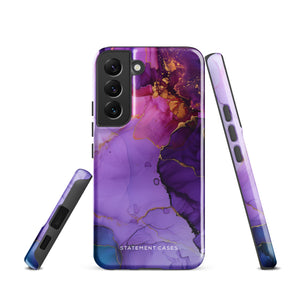 The Golden Orchid Marble for Samsung by Statement Cases is a smartphone adorned with a vibrant, abstract phone case showcasing a mix of purple, pink, and gold colors. Crafted from impact-resistant materials, it features a camera module with four lenses and a flash. At the bottom of the shock-absorbing phone case, you’ll find the text "STATEMENT CASES" in white.