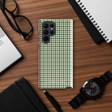 A smartphone with a green and white houndstooth patterned impact-resistant case is shown. The phone's camera module with multiple lenses is visible on the top left corner of the Elegance Houndstooth for Samsung shock-absorbing case by Statement Cases.
