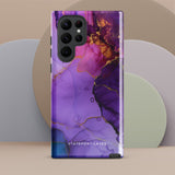 The Golden Orchid Marble for Samsung by Statement Cases is a smartphone adorned with a vibrant, abstract phone case showcasing a mix of purple, pink, and gold colors. Crafted from impact-resistant materials, it features a camera module with four lenses and a flash. At the bottom of the shock-absorbing phone case, you’ll find the text "STATEMENT CASES" in white.