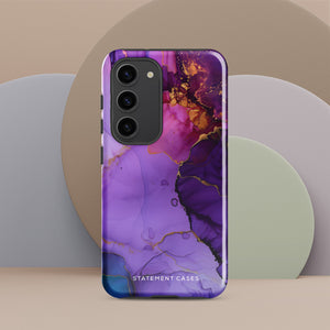 The Golden Orchid Marble for Samsung by Statement Cases is a smartphone adorned with a vibrant, abstract phone case showcasing a mix of purple, pink, and gold colors. Crafted from impact-resistant materials, it features a camera module with four lenses and a flash. At the bottom of the shock-absorbing phone case, you’ll find the text "STATEMENT CASES" in white.