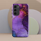 The Golden Orchid Marble for Samsung by Statement Cases is a smartphone adorned with a vibrant, abstract phone case showcasing a mix of purple, pink, and gold colors. Crafted from impact-resistant materials, it features a camera module with four lenses and a flash. At the bottom of the shock-absorbing phone case, you’ll find the text "STATEMENT CASES" in white.