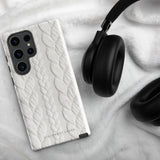 A stylish, impact-resistant phone case with a textured white braided design, covering the back of a smartphone. The dual-layer design features cutouts for the camera and buttons, and "Cozy Knit Bliss for Samsung" by Statement Cases is embossed at the bottom.