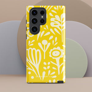 The Sol Dorado for Samsung by Statement Cases is a durable phone case featuring a bright yellow background adorned with an abstract white floral pattern, showcasing various flowers and leaves. Near the bottom edge, the text "STATEMENT CASE" highlights its dual-layer design for enhanced durability.