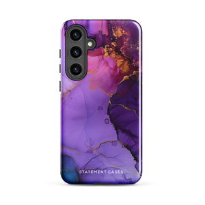 The Golden Orchid Marble for Samsung by Statement Cases is a smartphone adorned with a vibrant, abstract phone case showcasing a mix of purple, pink, and gold colors. Crafted from impact-resistant materials, it features a camera module with four lenses and a flash. At the bottom of the shock-absorbing phone case, you’ll find the text "STATEMENT CASES" in white.