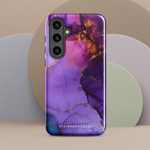 The Golden Orchid Marble for Samsung by Statement Cases is a smartphone adorned with a vibrant, abstract phone case showcasing a mix of purple, pink, and gold colors. Crafted from impact-resistant materials, it features a camera module with four lenses and a flash. At the bottom of the shock-absorbing phone case, you’ll find the text "STATEMENT CASES" in white.