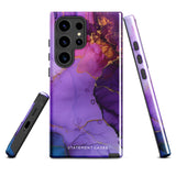 The Golden Orchid Marble for Samsung by Statement Cases is a smartphone adorned with a vibrant, abstract phone case showcasing a mix of purple, pink, and gold colors. Crafted from impact-resistant materials, it features a camera module with four lenses and a flash. At the bottom of the shock-absorbing phone case, you’ll find the text "STATEMENT CASES" in white.