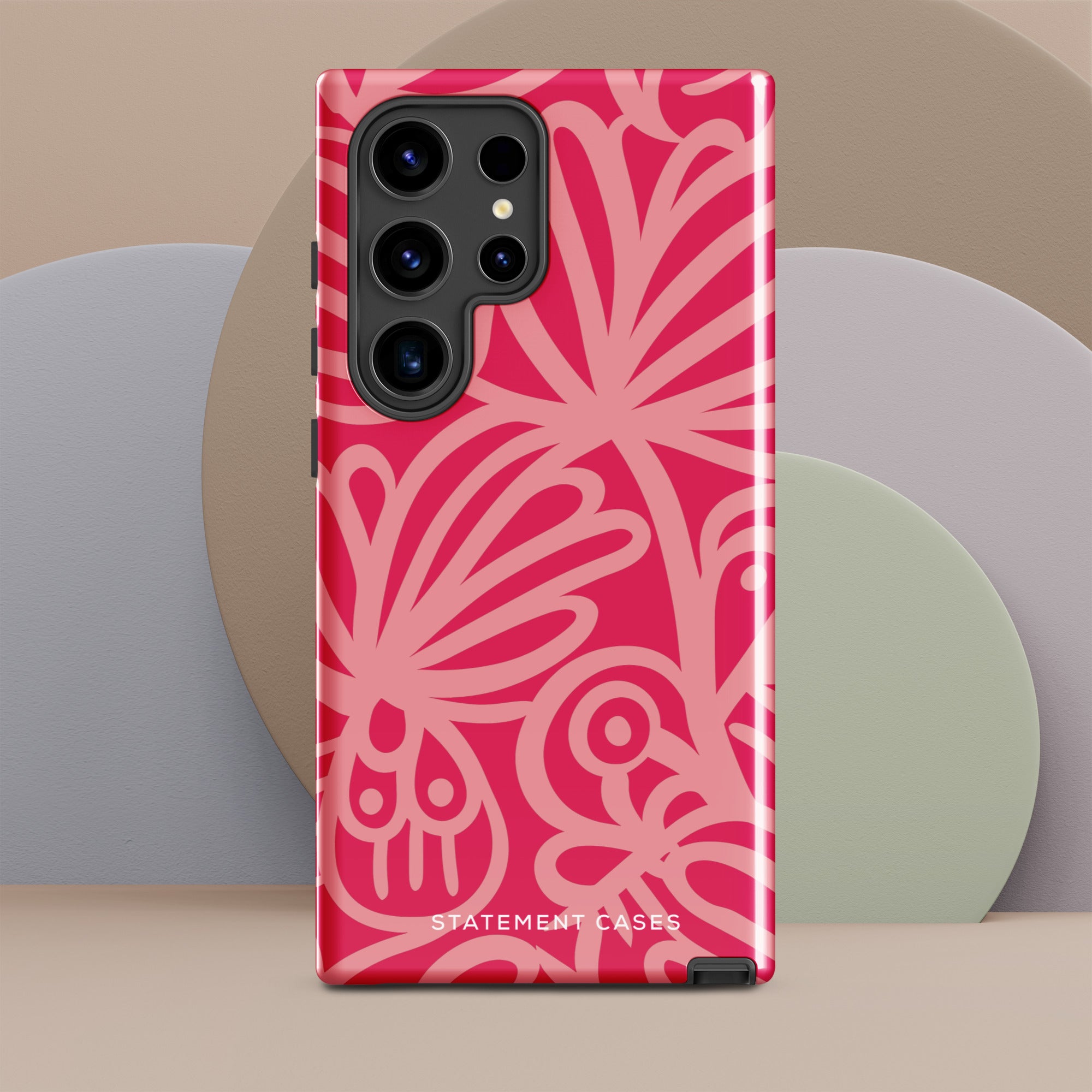 The Zafiro Rosa for Samsung, a smartphone from Statement Cases, comes with an impact-resistant pink floral-patterned case. The case showcases bold, abstract flower designs in various shades of pink and features the "STATEMENT CASES" text at the bottom. It also has a camera cutout that reveals multiple lenses, providing both style and protection.